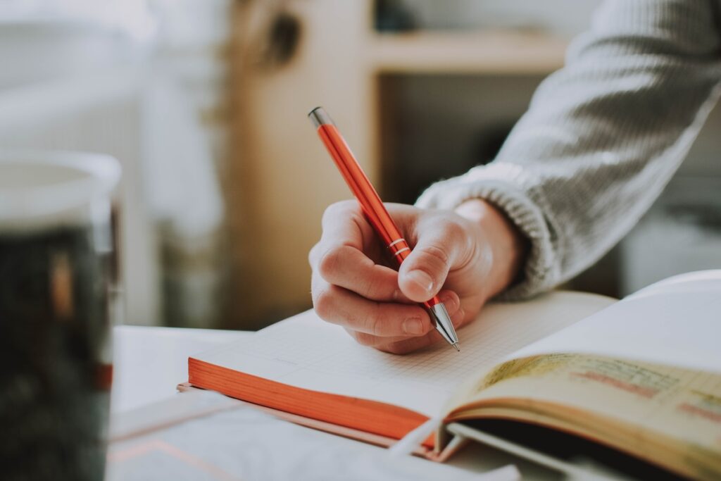 A person writing in a notebook with a pen.